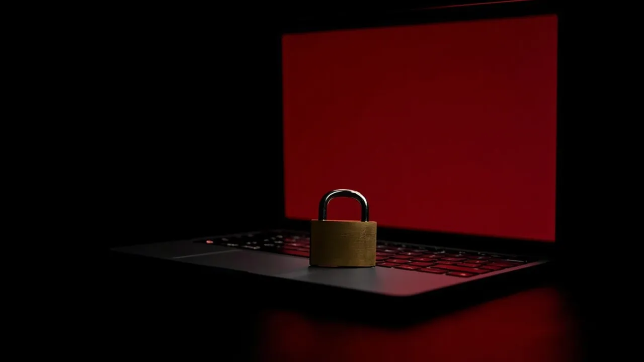 A small brass padlock resting on the keyboard of an open laptop whose screen glows crimson in a dark room