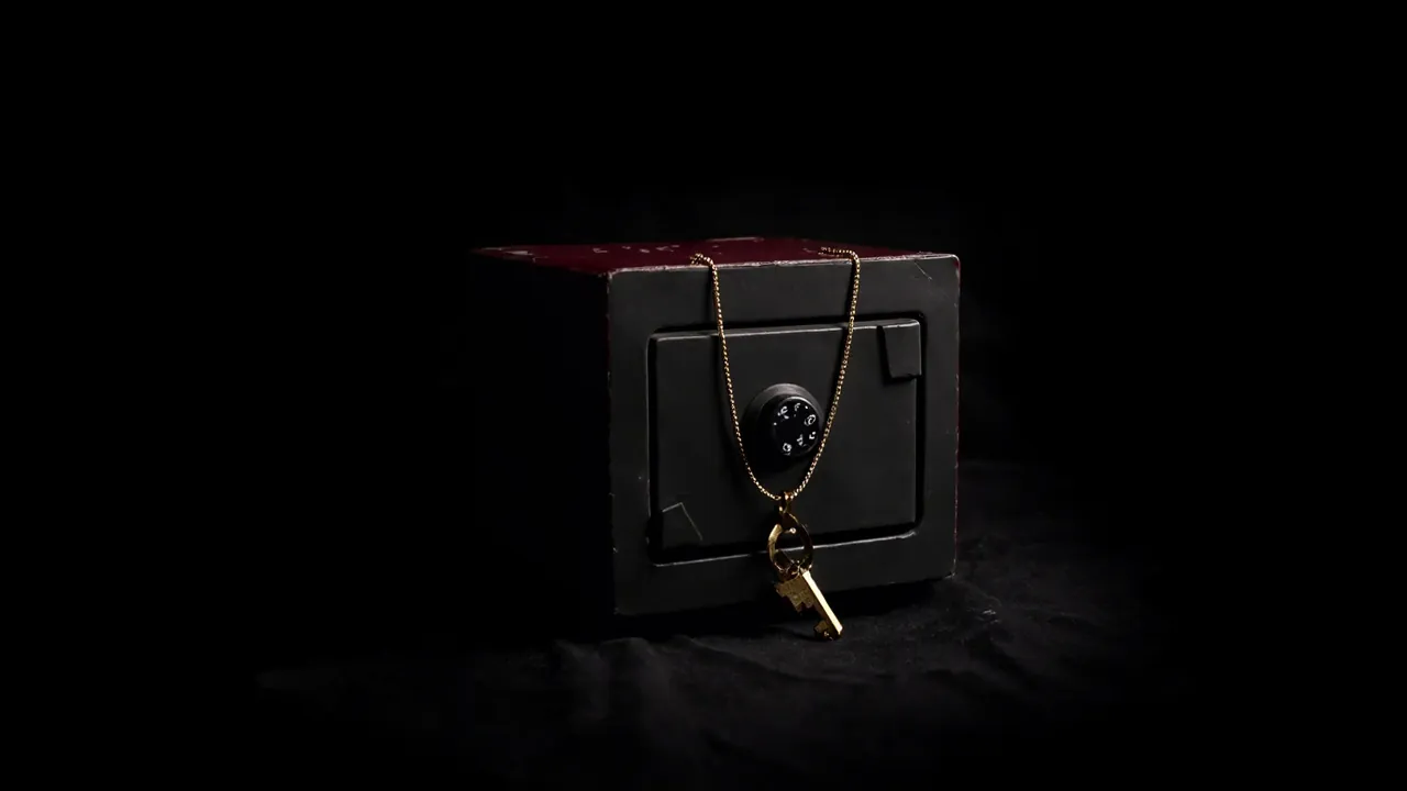A small black steel safe with a combination dial, a brass key on a fine gold chain draped over its lid