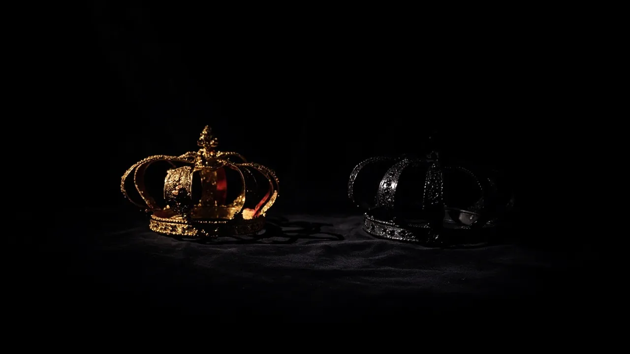 A gold crown and a black crown side by side on dark velvet