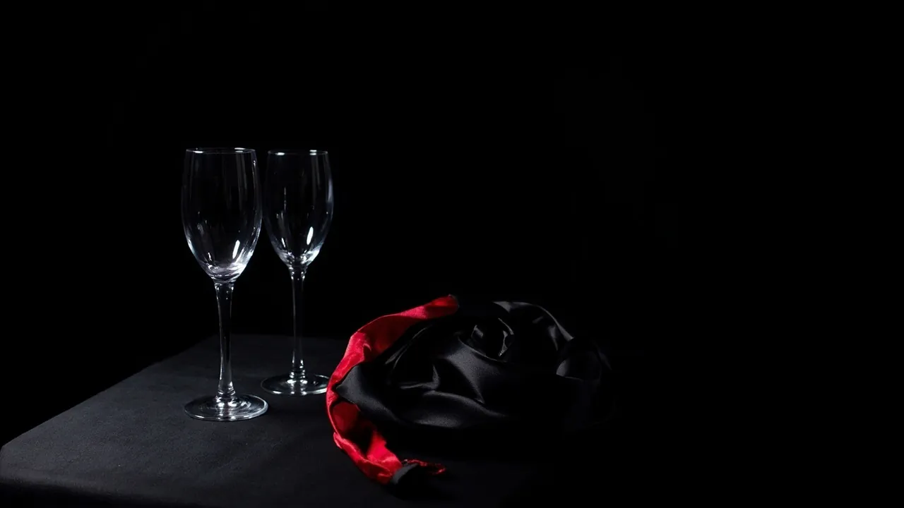 Two empty champagne glasses beside a black and red silk scarf on a dark table