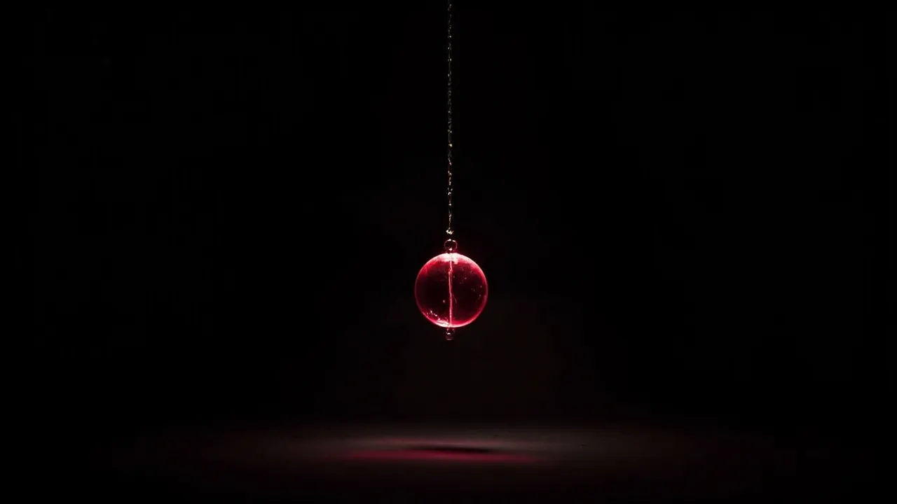 A red crystal pendulum hanging on a fine chain in the dark