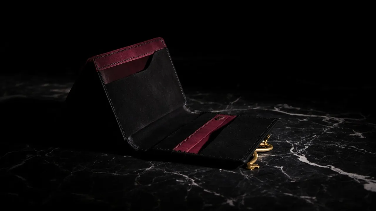 An open black leather wallet with a red lining and a small brass key on black marble