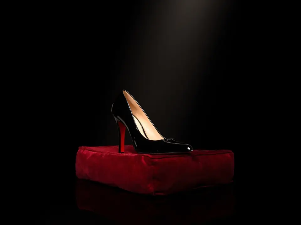 A black patent stiletto with a red sole on a crimson velvet cushion