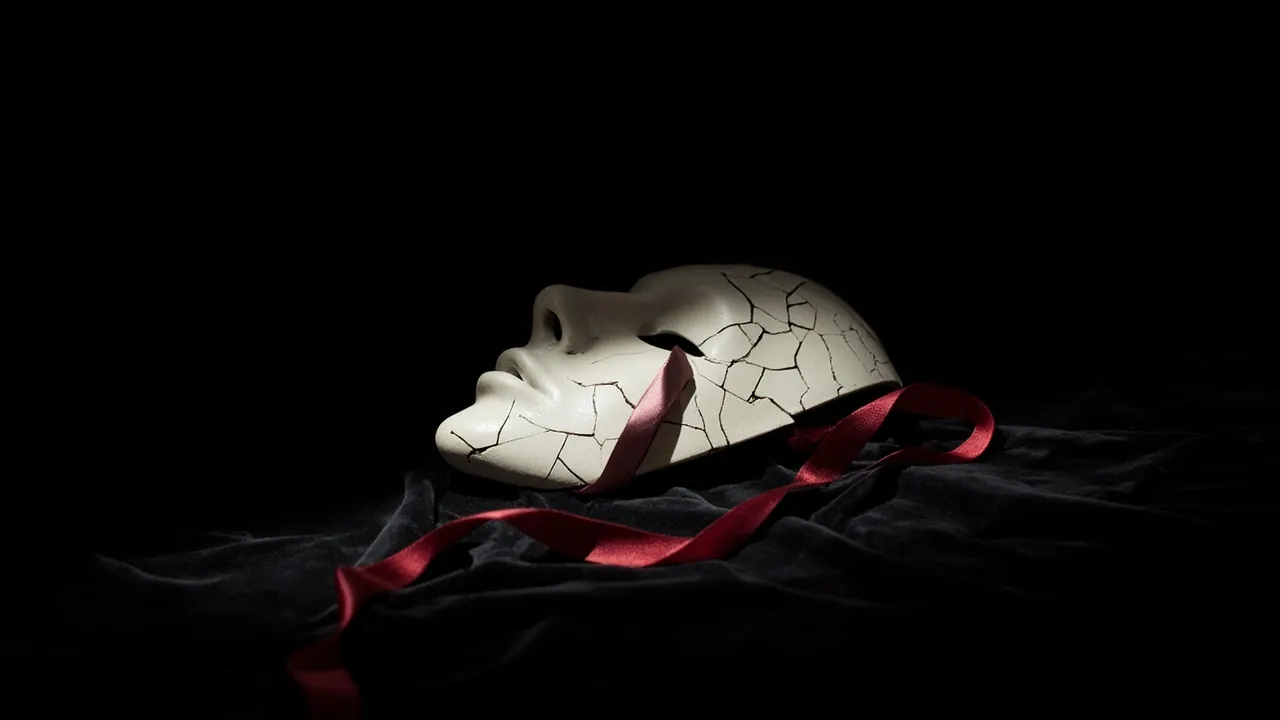 A cracked white theatre mask with a red ribbon on black velvet
