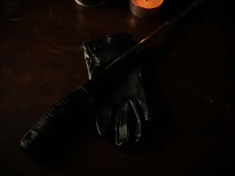 A leather riding crop across black leather gloves