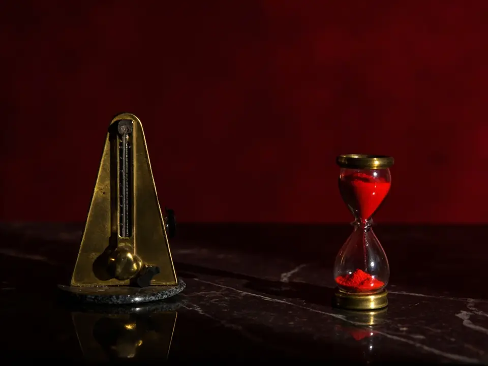 A brass metronome and an hourglass of red sand on black marble