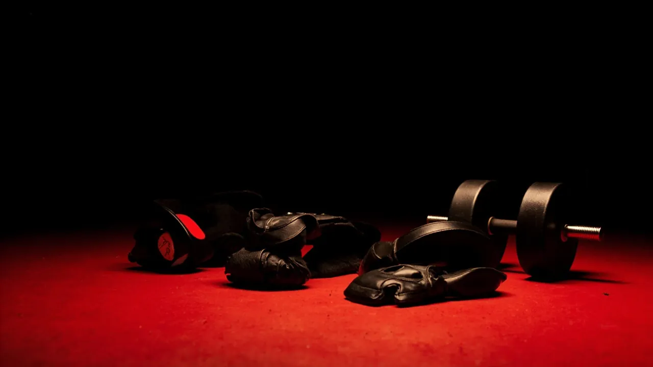 Black leather lifting gloves and a dumbbell on a red floor under a spotlight